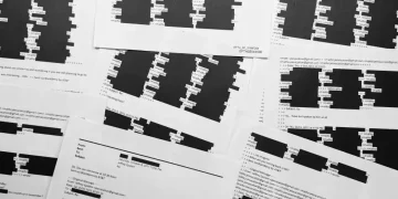 Court documents with redacted Epstein victims’ identities on a table - AP Photo/Jon Elswick