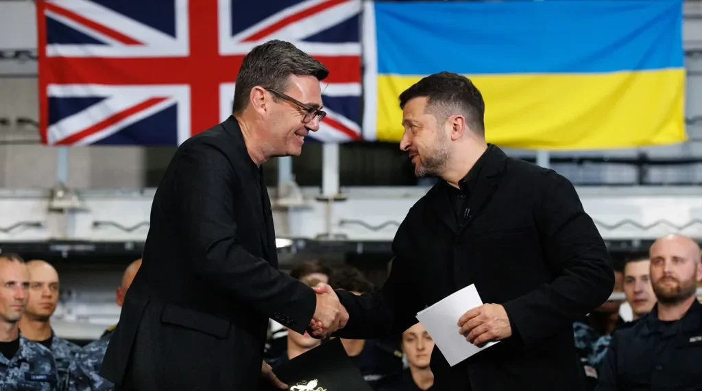 British Prime Minister Andy Burnham shakes hands with Ukrainian President Volodymyr Zelenskyy aboard HMS Queen Elizabeth in Portsmouth, with British and Ukrainian flags in the background.