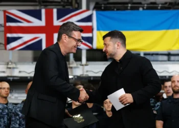 British Prime Minister Andy Burnham shakes hands with Ukrainian President Volodymyr Zelenskyy aboard HMS Queen Elizabeth in Portsmouth, with British and Ukrainian flags in the background.