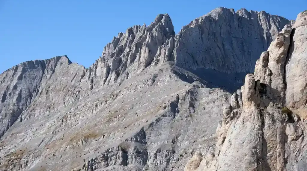 Mountain landscape in Olympus National Park, Greece, showing forested slopes, rocky peaks, and natural scenery beneath a clear sky.