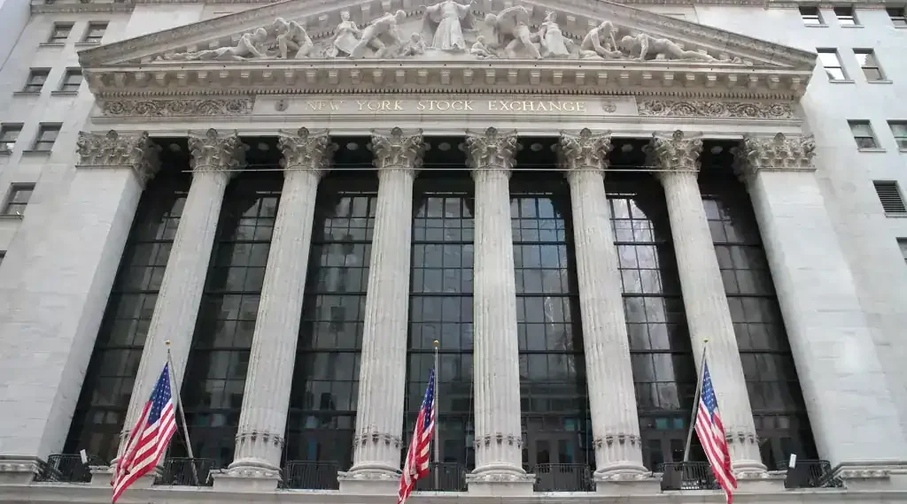 Exterior view of the New York Stock Exchange building on Wall Street in New York City's Financial District, displaying its neoclassical façade and American flags.