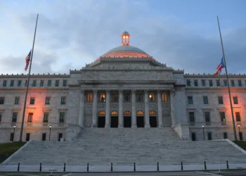 The Capitol of Puerto Rico overlooks San Juan Bay at dusk with the United States and Puerto Rico flags flying at half-staff.