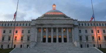 The Capitol of Puerto Rico overlooks San Juan Bay at dusk with the United States and Puerto Rico flags flying at half-staff.