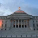 The Capitol of Puerto Rico overlooks San Juan Bay at dusk with the United States and Puerto Rico flags flying at half-staff.