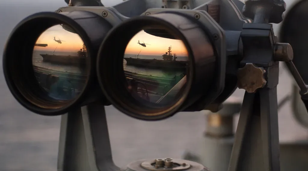 A pair of binoculars sits on the signal bridge of USS Harry S. Truman as an MH-60S Seahawk conducts a replenishment mission at sea.