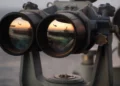 A pair of binoculars sits on the signal bridge of USS Harry S. Truman as an MH-60S Seahawk conducts a replenishment mission at sea.