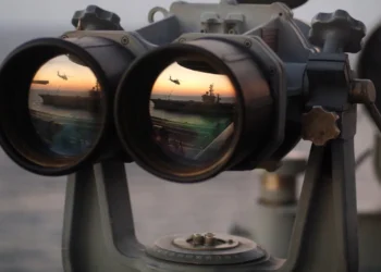 A pair of binoculars sits on the signal bridge of USS Harry S. Truman as an MH-60S Seahawk conducts a replenishment mission at sea.