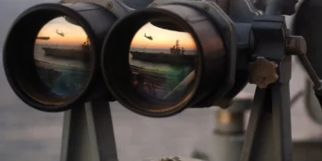 A pair of binoculars sits on the signal bridge of USS Harry S. Truman as an MH-60S Seahawk conducts a replenishment mission at sea.