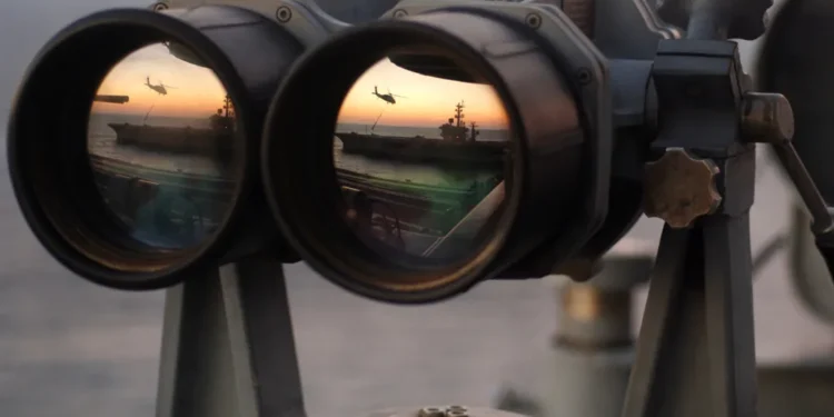 A pair of binoculars sits on the signal bridge of USS Harry S. Truman as an MH-60S Seahawk conducts a replenishment mission at sea.