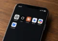 Smartphone displaying ChatGPT, Grok, Claude, Gemini, Copilot and DeepSeek apps on a wooden surface.