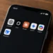 Smartphone displaying ChatGPT, Grok, Claude, Gemini, Copilot and DeepSeek apps on a wooden surface.