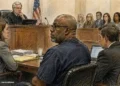 Courtroom illustration showing a defendant seated with lawyers before a judge, with attorneys and court observers visible in the background.