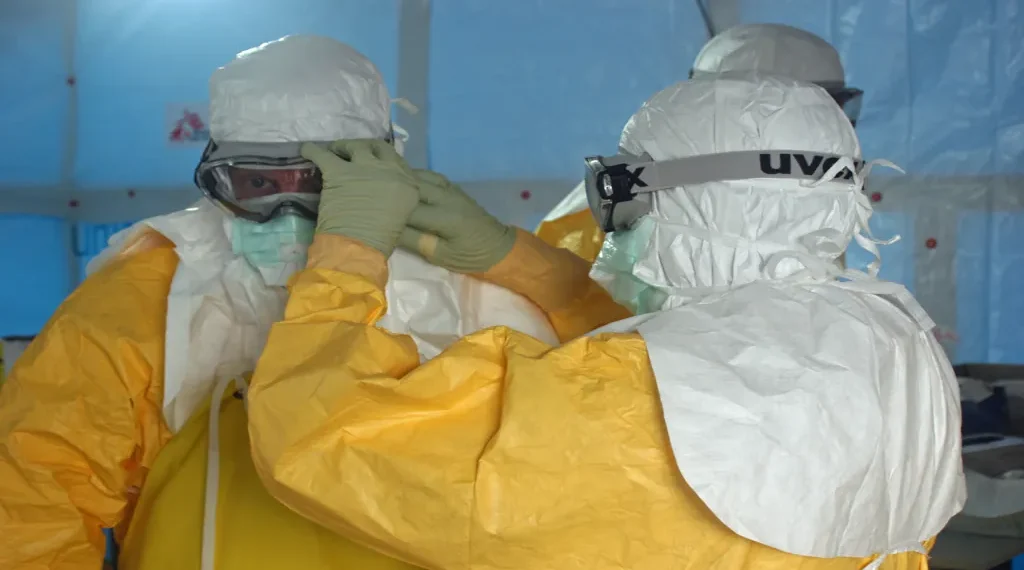 MSF staff member helps a CDC doctor secure his face mask before entering an Ebola treatment unit in Liberia.