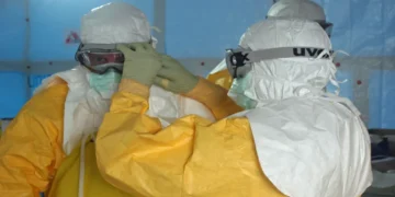 MSF staff member helps a CDC doctor secure his face mask before entering an Ebola treatment unit in Liberia.