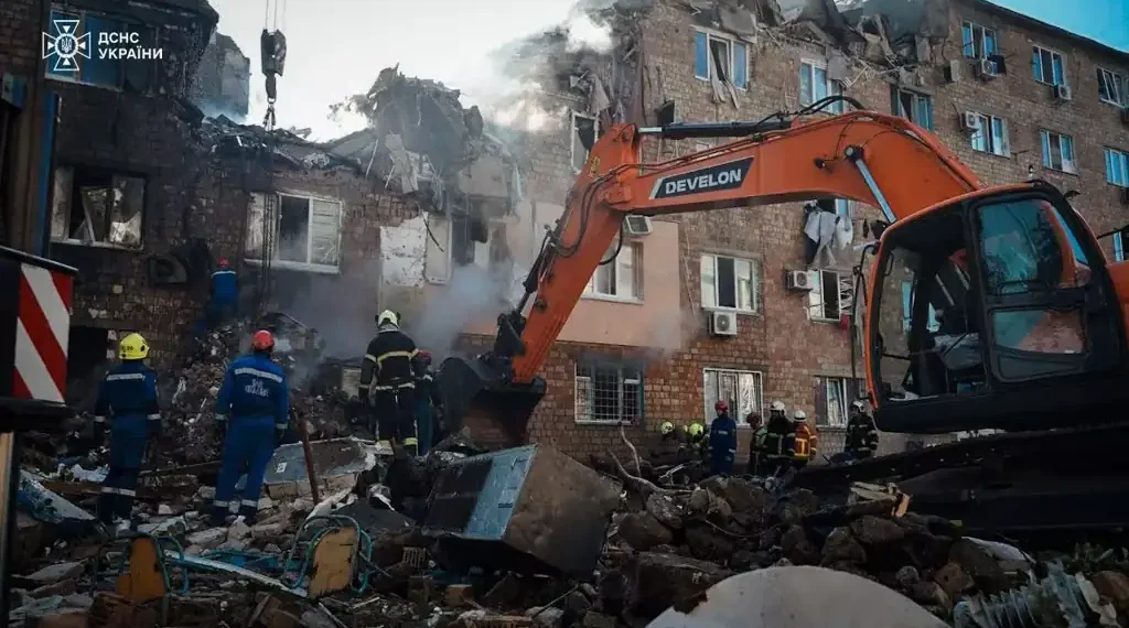 Ukrainian emergency responders work among rubble beside an excavator at a heavily damaged apartment building in Kyiv.