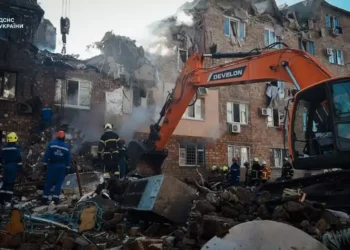 Ukrainian emergency responders work among rubble beside an excavator at a heavily damaged apartment building in Kyiv.