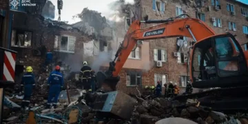 Ukrainian emergency responders work among rubble beside an excavator at a heavily damaged apartment building in Kyiv.