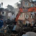 Ukrainian emergency responders work among rubble beside an excavator at a heavily damaged apartment building in Kyiv.