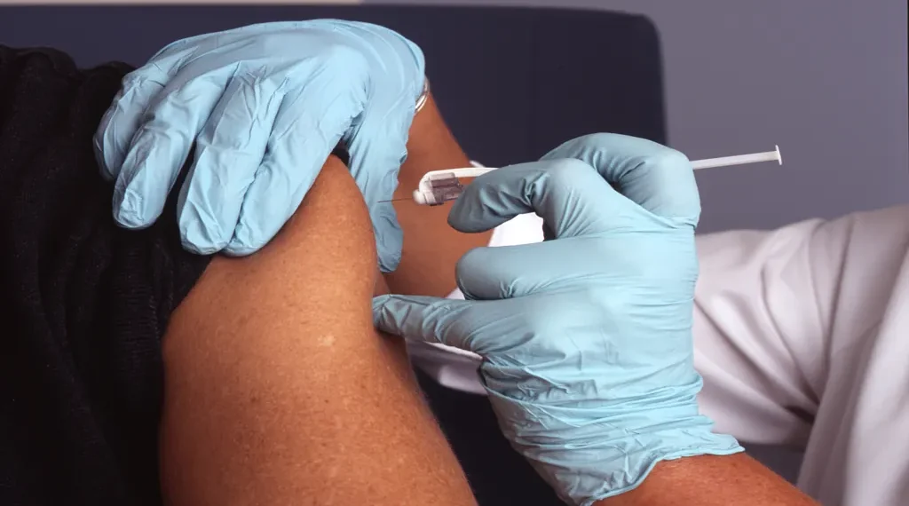 A nurse wearing protective gloves administers a vaccine injection into an adult patient's upper arm during an immunization appointment.