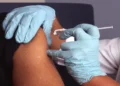 A nurse wearing protective gloves administers a vaccine injection into an adult patient's upper arm during an immunization appointment.