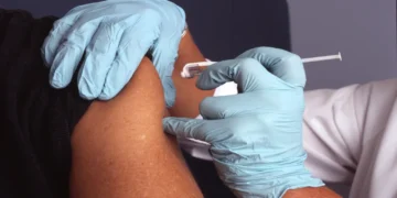 A nurse wearing protective gloves administers a vaccine injection into an adult patient's upper arm during an immunization appointment.