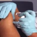 A nurse wearing protective gloves administers a vaccine injection into an adult patient's upper arm during an immunization appointment.
