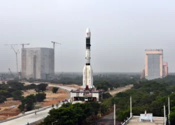 GSLV-F08 rocket stands on a mobile launch pedestal with the Vehicle Assembly Building visible behind it at an ISRO launch complex.