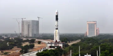 GSLV-F08 rocket stands on a mobile launch pedestal with the Vehicle Assembly Building visible behind it at an ISRO launch complex.