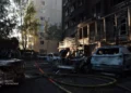 Damaged apartment building and burned vehicles at a Kyiv attack site as a person works among debris and emergency hoses.