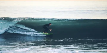 Surfer rides a large ocean wave at 54th Street in Newport Beach, California, with breaking whitewater surrounding the surfer.
