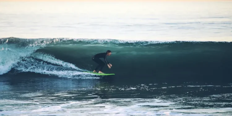 Surfer rides a large ocean wave at 54th Street in Newport Beach, California, with breaking whitewater surrounding the surfer.