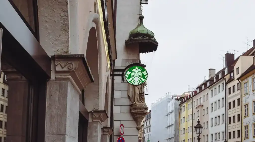 Starbucks siren sign stands before an Archangel Michael statue on Sendlinger Straße in Munich, Germany.