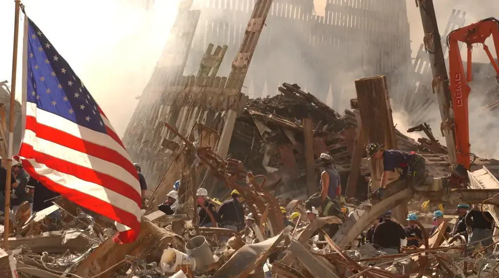 Rescue workers search through World Trade Center rubble beneath an American flag in New York City after the September 11 attacks.