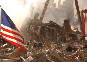 Rescue workers search through World Trade Center rubble beneath an American flag in New York City after the September 11 attacks.