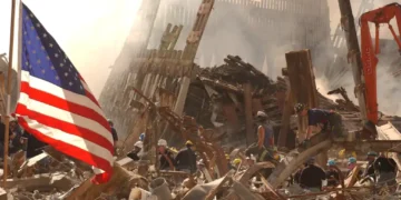 Rescue workers search through World Trade Center rubble beneath an American flag in New York City after the September 11 attacks.