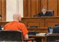 Defendant in orange jail clothing sits before a judge during a courtroom proceeding, with attorneys and a sheriff's deputy nearby.