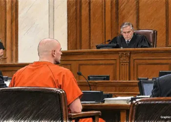 Defendant in orange jail clothing sits before a judge during a courtroom proceeding, with attorneys and a sheriff's deputy nearby.