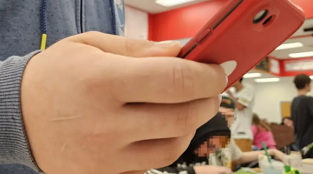 Teenager holding a red second-generation iPhone SE, photographed on May 22, 2024.