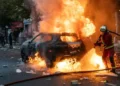 Firefighters extinguish a burning car during protests and riots in Paris, France, on October 17, 2026, amid smoke and unrest.