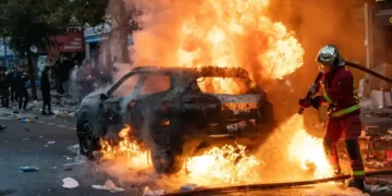 Firefighters extinguish a burning car during protests and riots in Paris, France, on October 17, 2026, amid smoke and unrest.